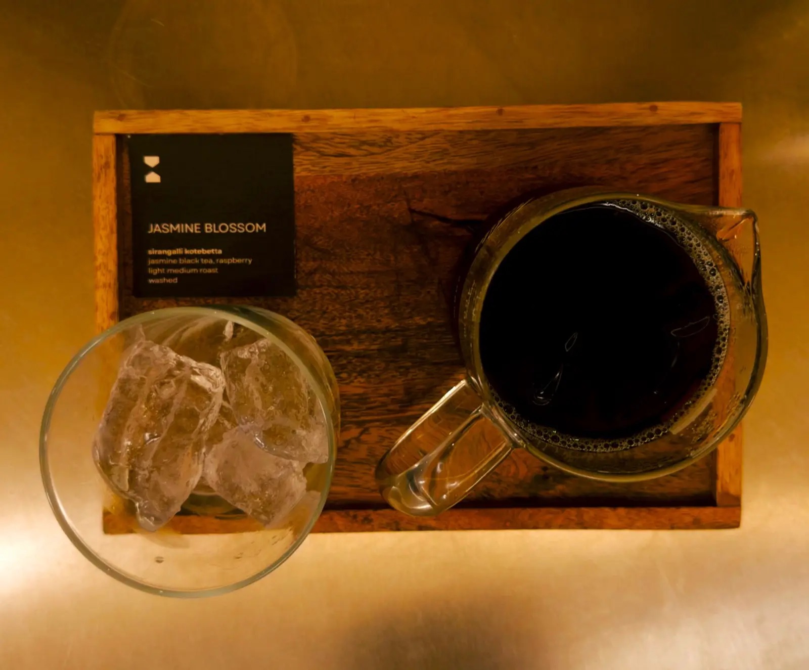 A cup of black coffee and a glass of water on a wooden tray